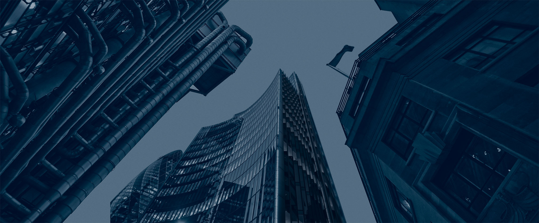 Upward view of skyscrapers and industrial-style building exteriors against sky, blue-toned duotone, corporate and composed mood
